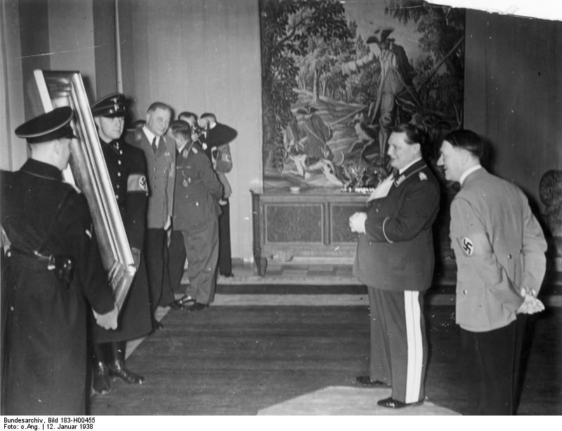 Hitler überreicht Hermann Göring (1893–1946) zu seinem 45. Geburtstag am 12. Januar 1938 ein Gemälde. Ebenso wie Göring, der seine private Kunstsammlung großteils aus geraubten und abgepressten Kunstwerken aufbaute, war auch Hitler für seine Sammelleidenschaft berüchtigt. So sollte etwa im Rahmen des „Sonderauftrag Linz“ ein „Führermuseum“ entstehen, für das europaweit große Mengen an wertvollen Kunst- und Kulturgüter zusammengerafft wurden, Wikimedia Commons, CC BY-SA 3.0.