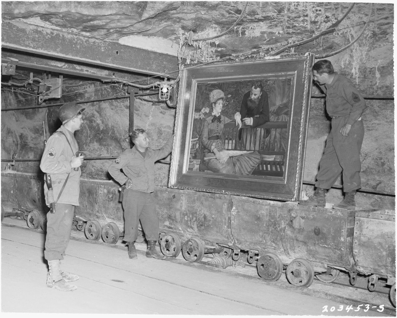 In der Salzmine von Merkers (Thüringen) fand die US-Armee im Frühjahr 1945 unüberschaubare Mengen an Wertgegenständen – neben Kunstwerken der Berliner Museen auch Raubgut der SS und umfangreiche Goldreserven der Reichsbank. Das Foto zeigt amerikanische Soldaten mit dem 1879 entstandenen Bild „Im Wintergarten“ von Édouard Manet, das heute wieder in der Alten Nationalgalerie der Staatlichen Museen zu Berlin – Preußischer Kulturbesitz ausgestellt ist, Wikimedia Commons, Gemeinfrei.