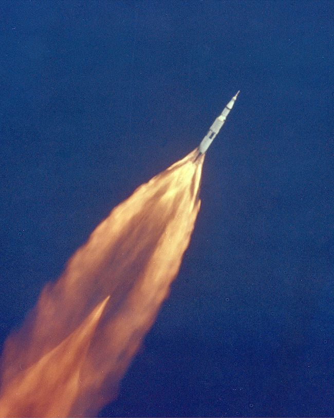 Foto: The Apollo 11 Saturn V space vehicle climbs toward orbit after liftoff from Pad 39A at 9:32 a.m. EDT. In 2 1/2 minutes of powered flight, the S-IC booster lifts the vehicle to an altitude of about 39 miles some 55 miles downrange. This photo was taken with a 70mm telescopic camera mounted in an Air Force EC-135N plane. Onboard are astronauts Neil A. Armstrong, Michael Collins and Edwin E. Aldrin, Jr.Original Source: NASA. Quelle: Wikimedia Commons. Public Domain.