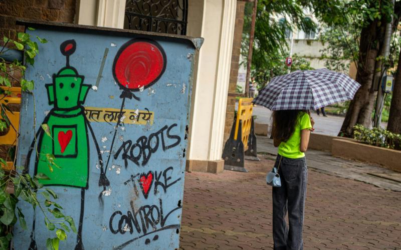 Links ein Graffiti mit der Aufschrift "Robots take control", rechts eine junge Frau mit Regenschirm