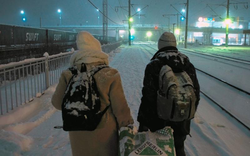 Ein Paar geht in einer verschneiten Winterlandschaft an Eisenbahngleisen entlang