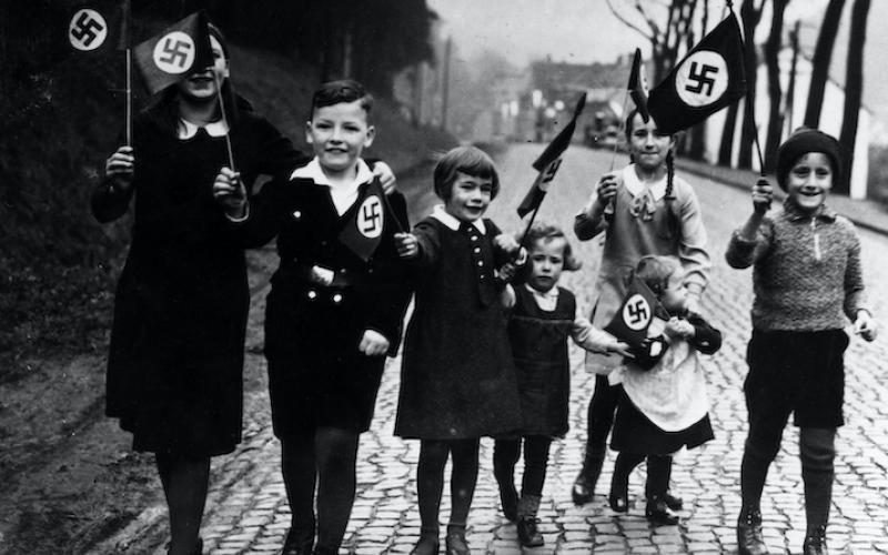 Kinder gehen mit Hakenkreuzfahnen in der Hand spazieren. Propagandafoto für die Presse