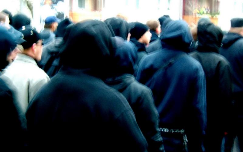 Rückansicht von Menschen mit schwarzen Kapuzen beim Nazi-Aufmarsch und Gegendemo