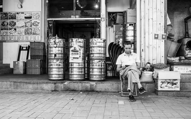 Schwarzweißfoto eines vor einem Biergeschäft sitzenden Mannes in Qingdao
