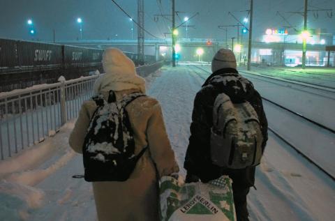 Ein Paar geht in einer verschneiten Winterlandschaft an Eisenbahngleisen entlang