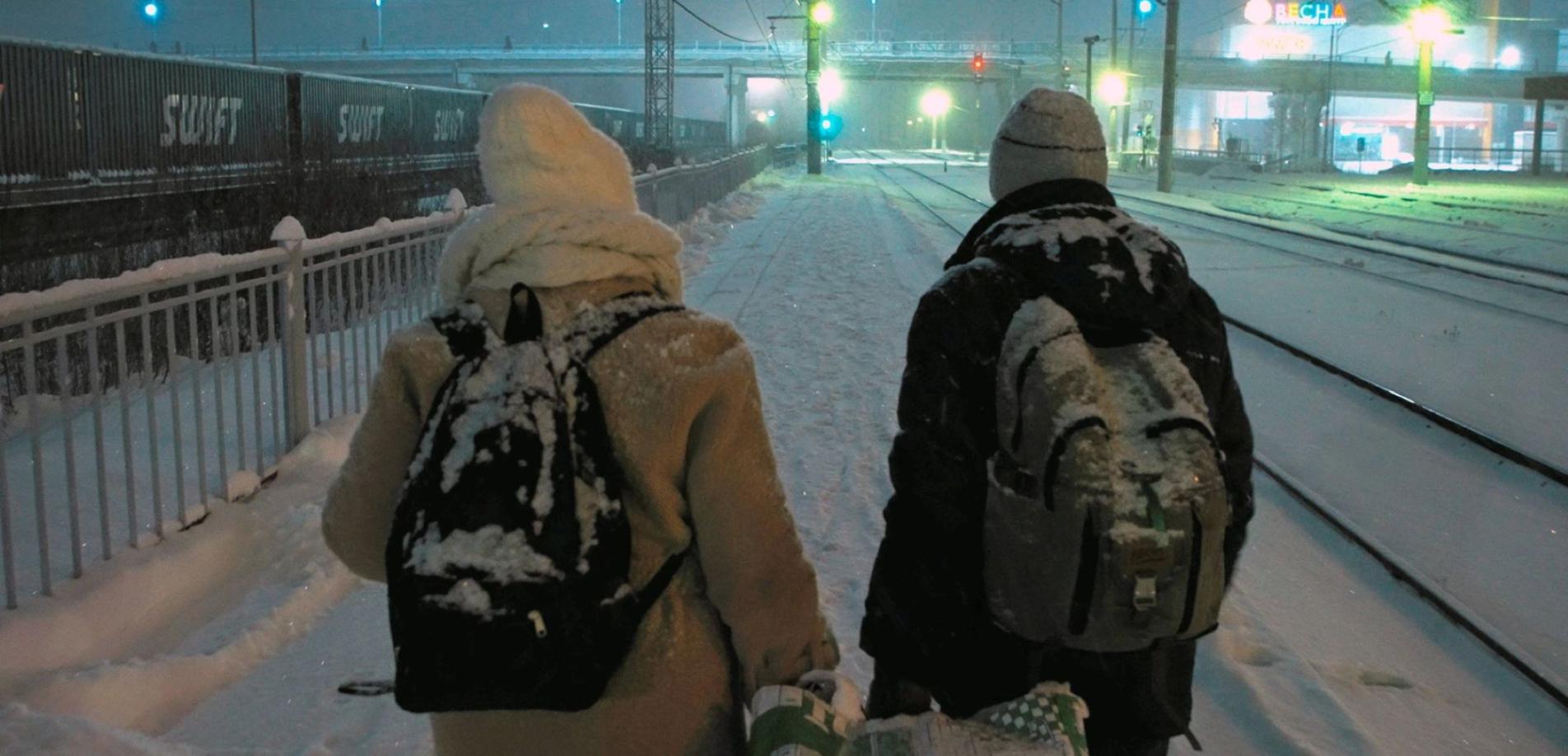 Ein Paar geht in einer verschneiten Winterlandschaft an Eisenbahngleisen entlang