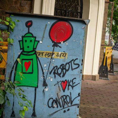 Links ein Graffiti mit der Aufschrift "Robots take control", rechts eine junge Frau mit Regenschirm