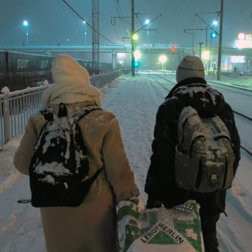 Ein Paar geht in einer verschneiten Winterlandschaft an Eisenbahngleisen entlang