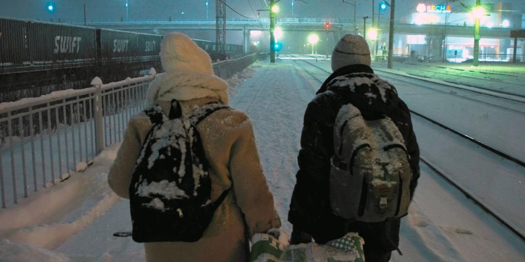 Ein Paar geht in einer verschneiten Winterlandschaft an Eisenbahngleisen entlang