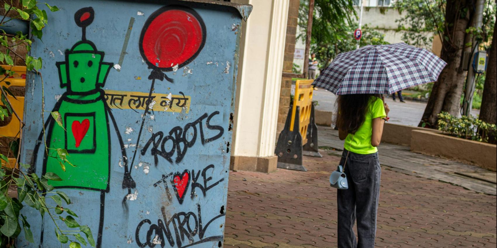 Links ein Graffiti mit der Aufschrift "Robots take control", rechts eine junge Frau mit Regenschirm