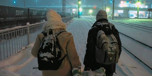 Ein Paar geht in einer verschneiten Winterlandschaft an Eisenbahngleisen entlang