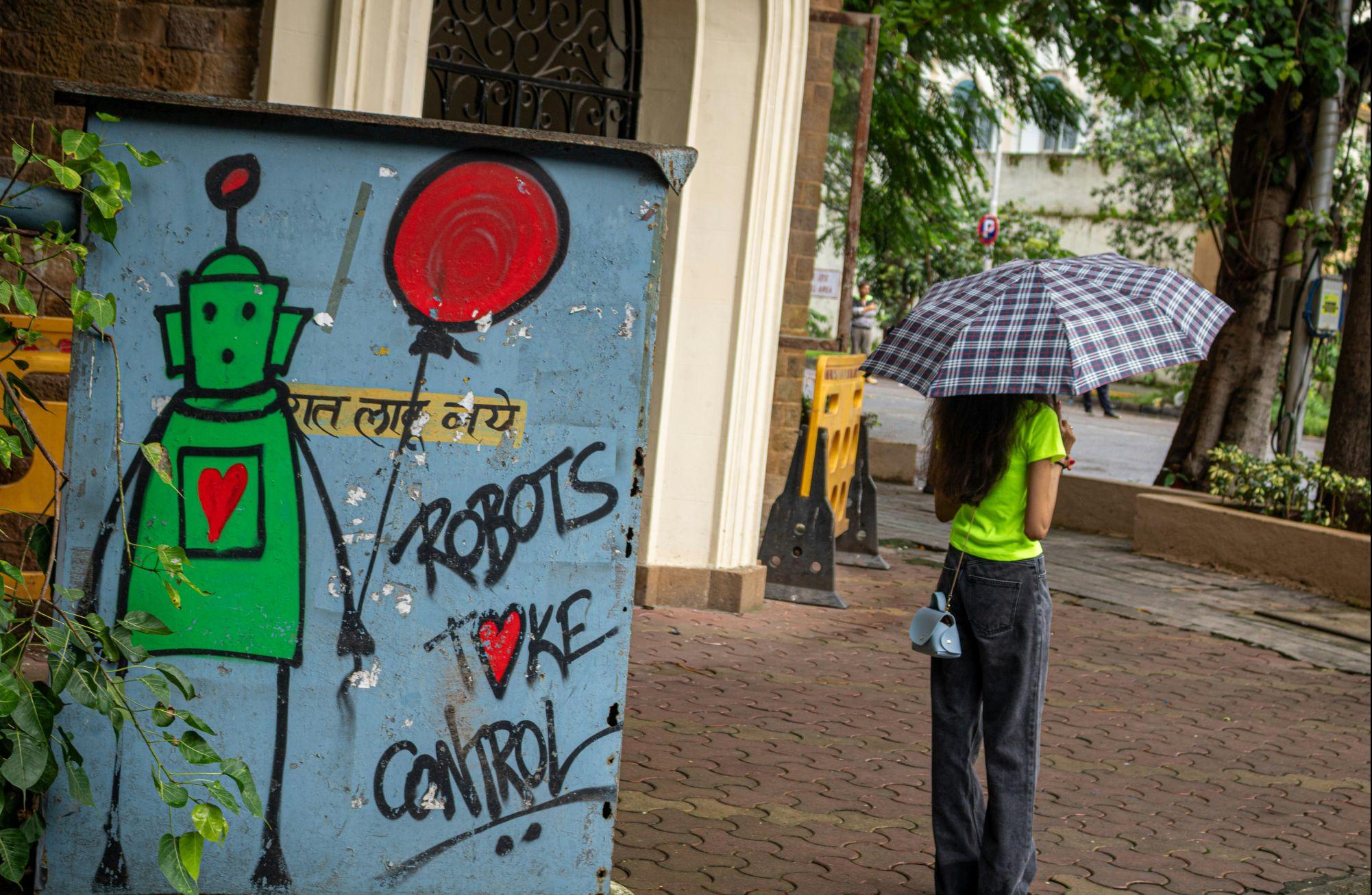 Links ein Graffiti mit der Aufschrift "Robots take control", rechts eine junge Frau mit Regenschirm